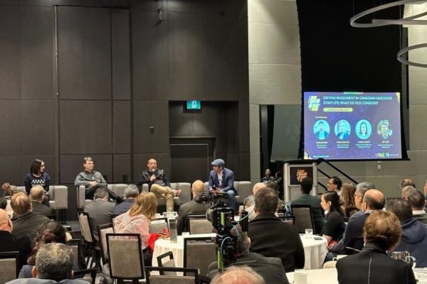 Panelist on stage at VentureLab's Hard Tech conference with attendees sitting at round tables