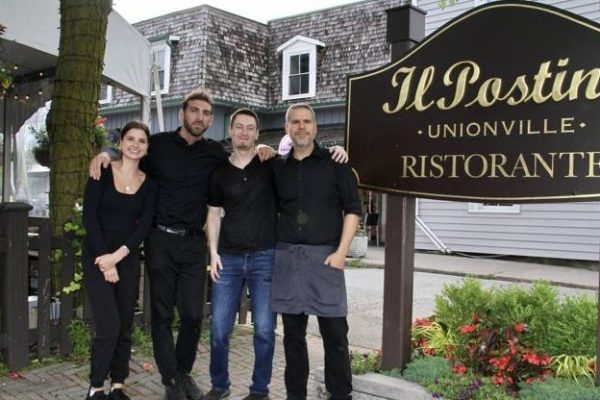 Restaurant staff at Il Postino standing in front of sign outside